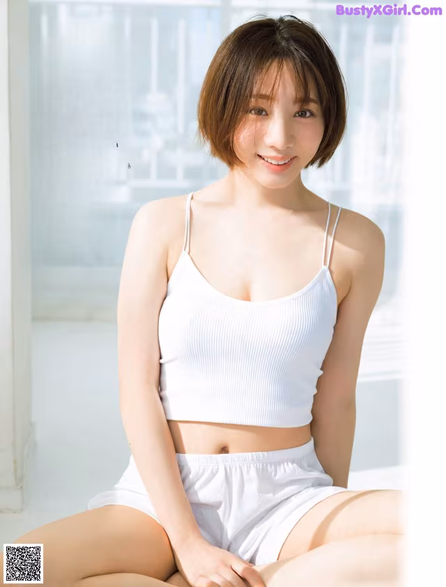 A woman in a white top and shorts sitting on the floor.