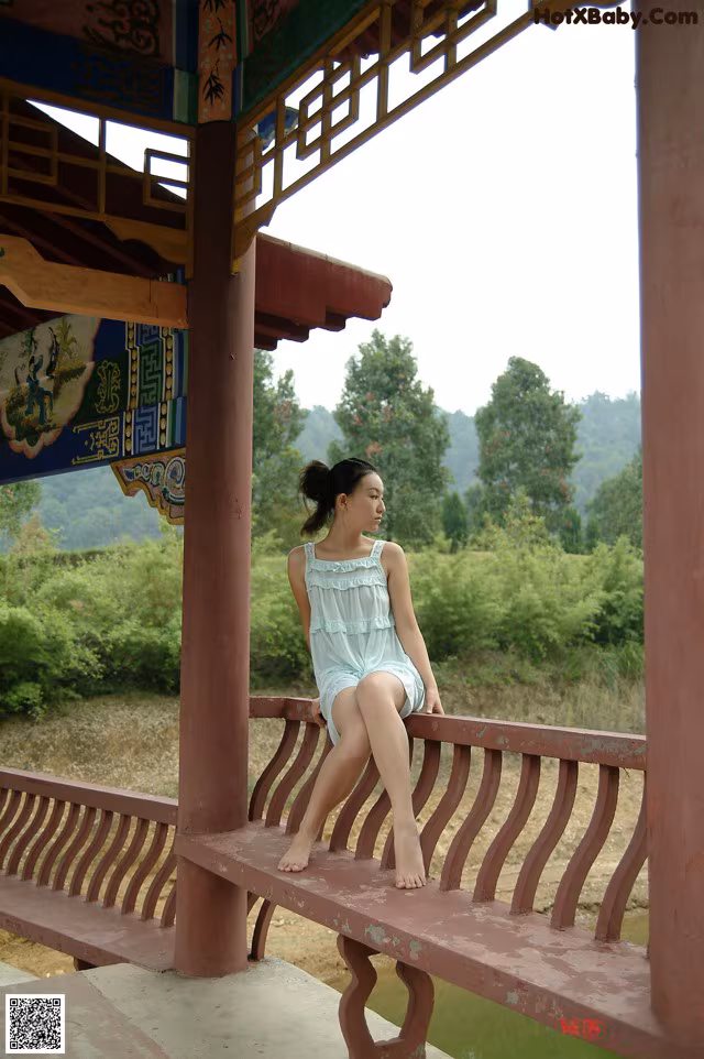 A woman sitting on a wooden bench in a pavilion.