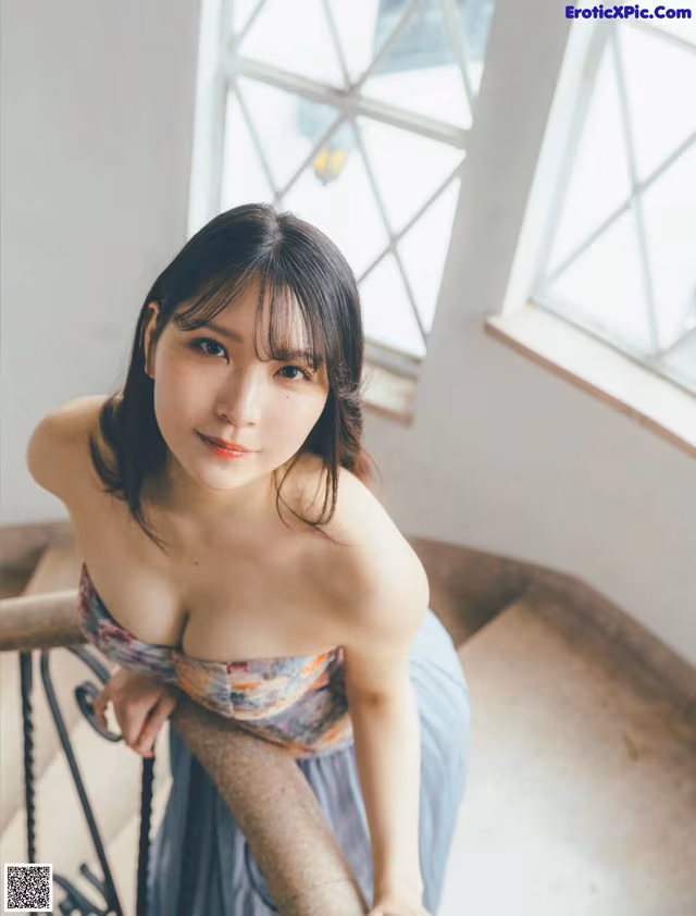 A woman in a blue dress leaning against a railing.