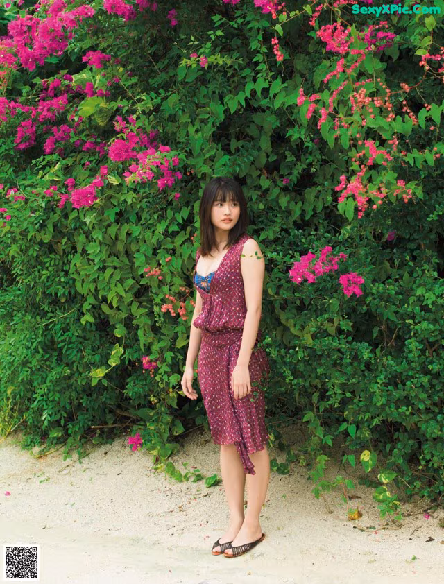 A woman standing in front of a bush of pink flowers.