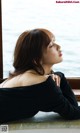 A woman leaning against a window looking out at the ocean.