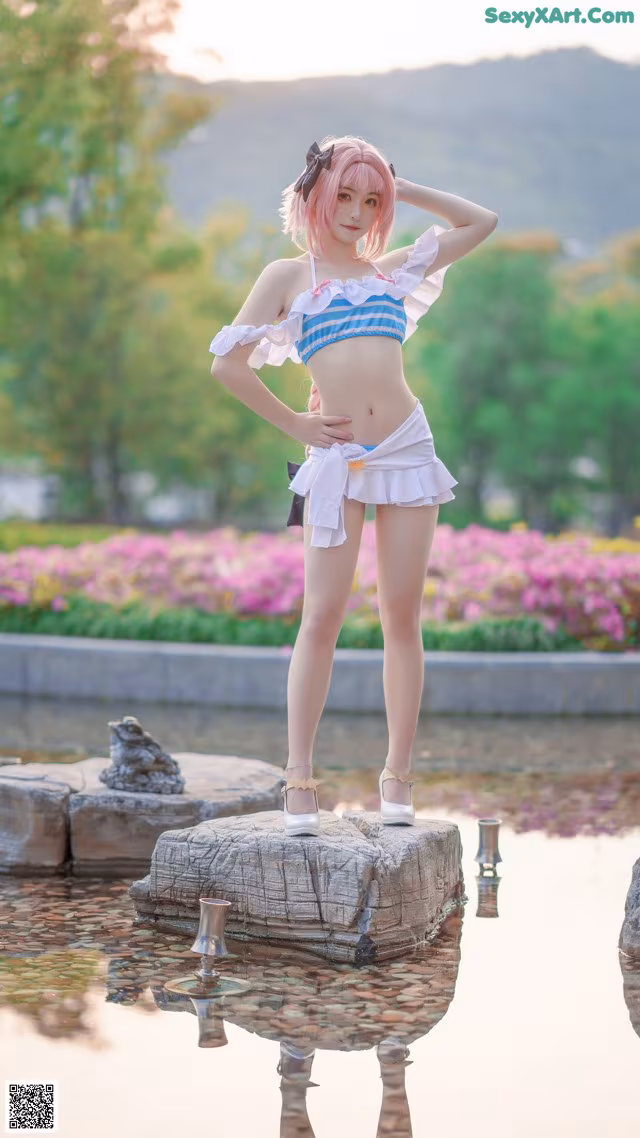 A woman in a bikini standing on a rock by a pond.