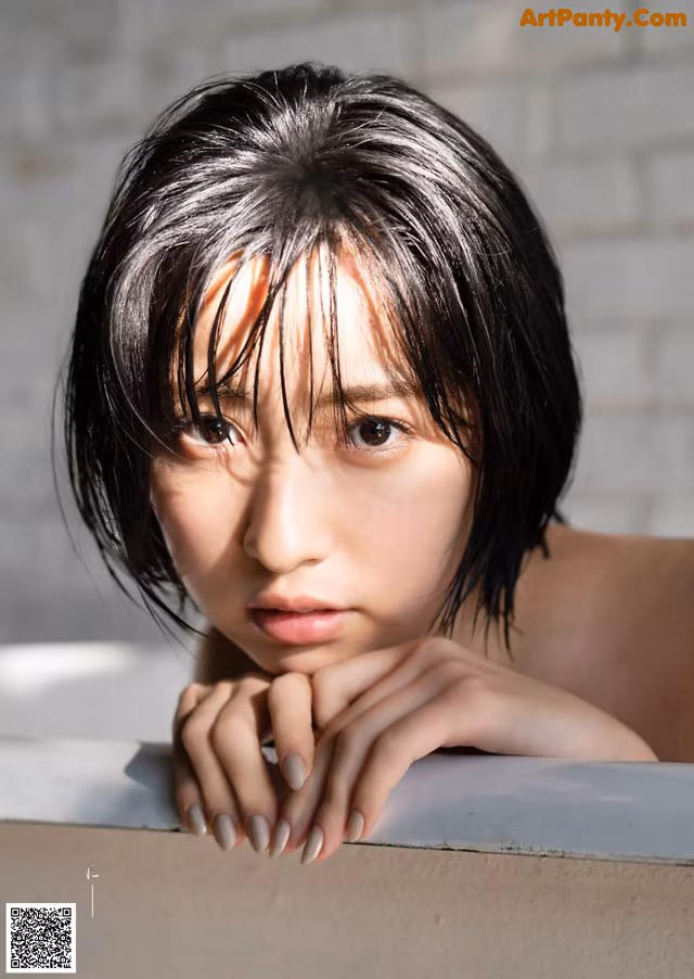 A woman leaning against a wall with her hand on her chin.