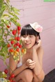 A young woman sitting on the ground next to a tomato plant.