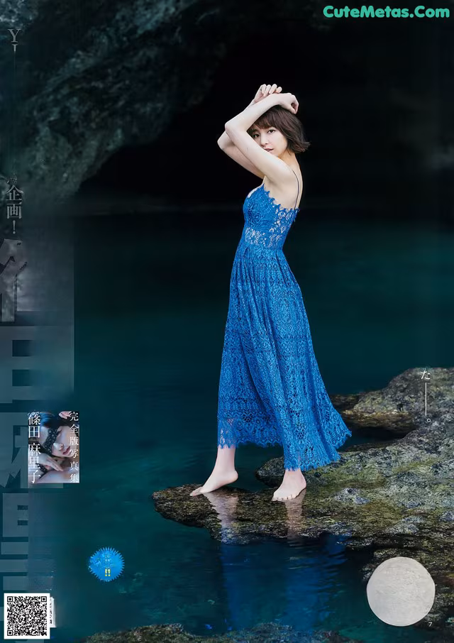 A woman in a blue dress standing on a rock in the water.