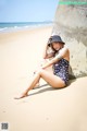 A woman sitting on a beach next to a rock.