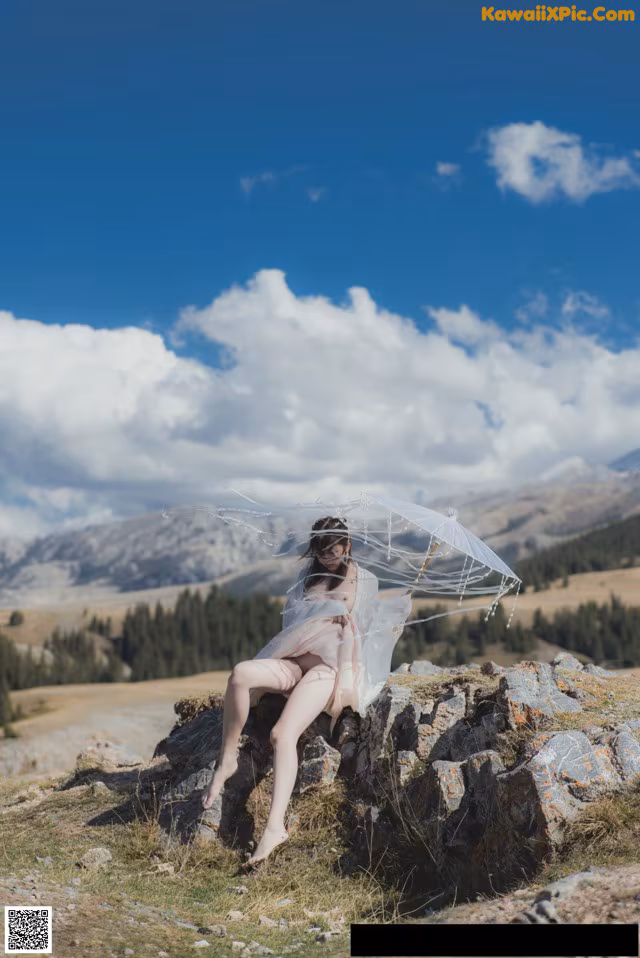 A woman sitting on top of a rock holding an umbrella.