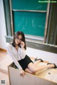 A woman sitting on top of a desk next to a blackboard.